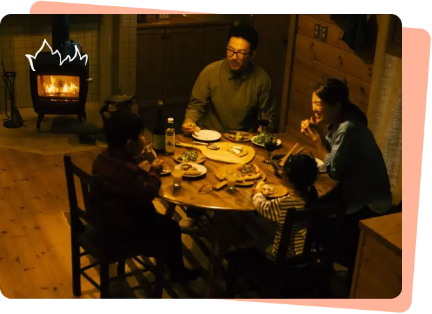 薪ストーブが灯る部屋で食事を囲う家族の画像